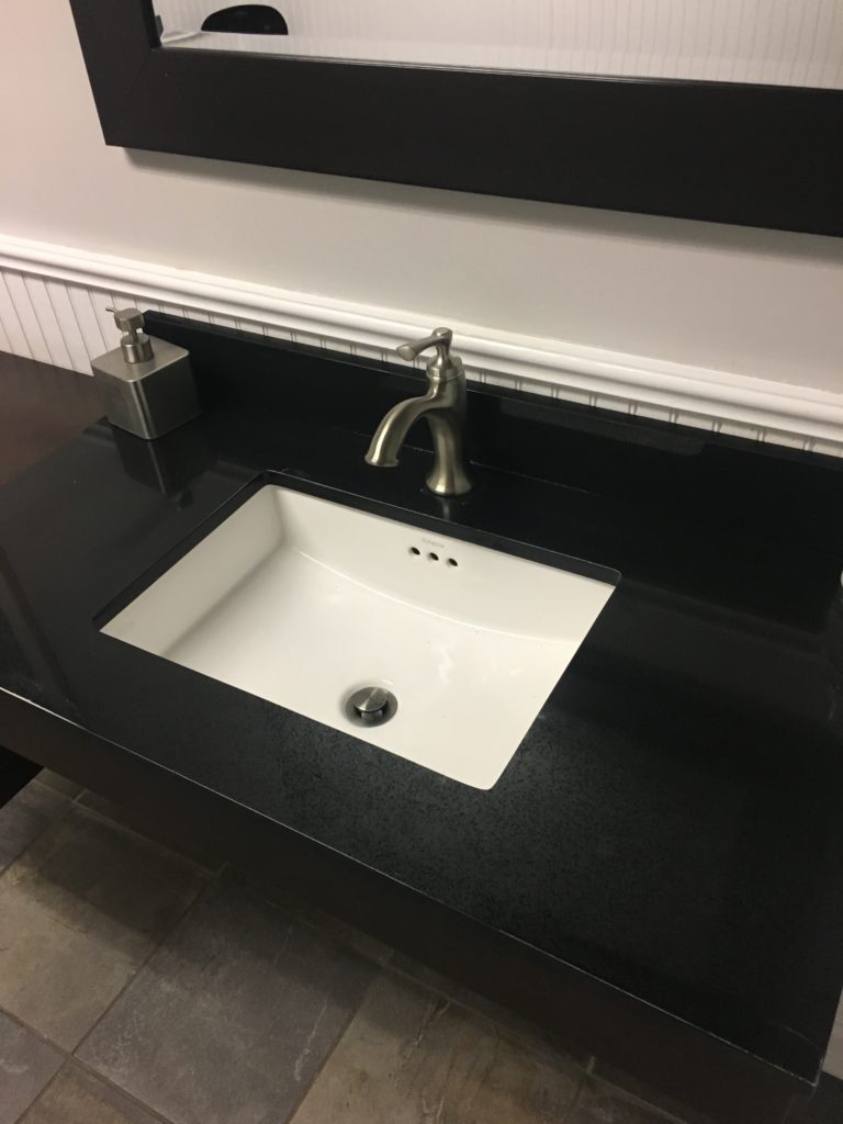 A bathroom sink with black counter top and white tile.