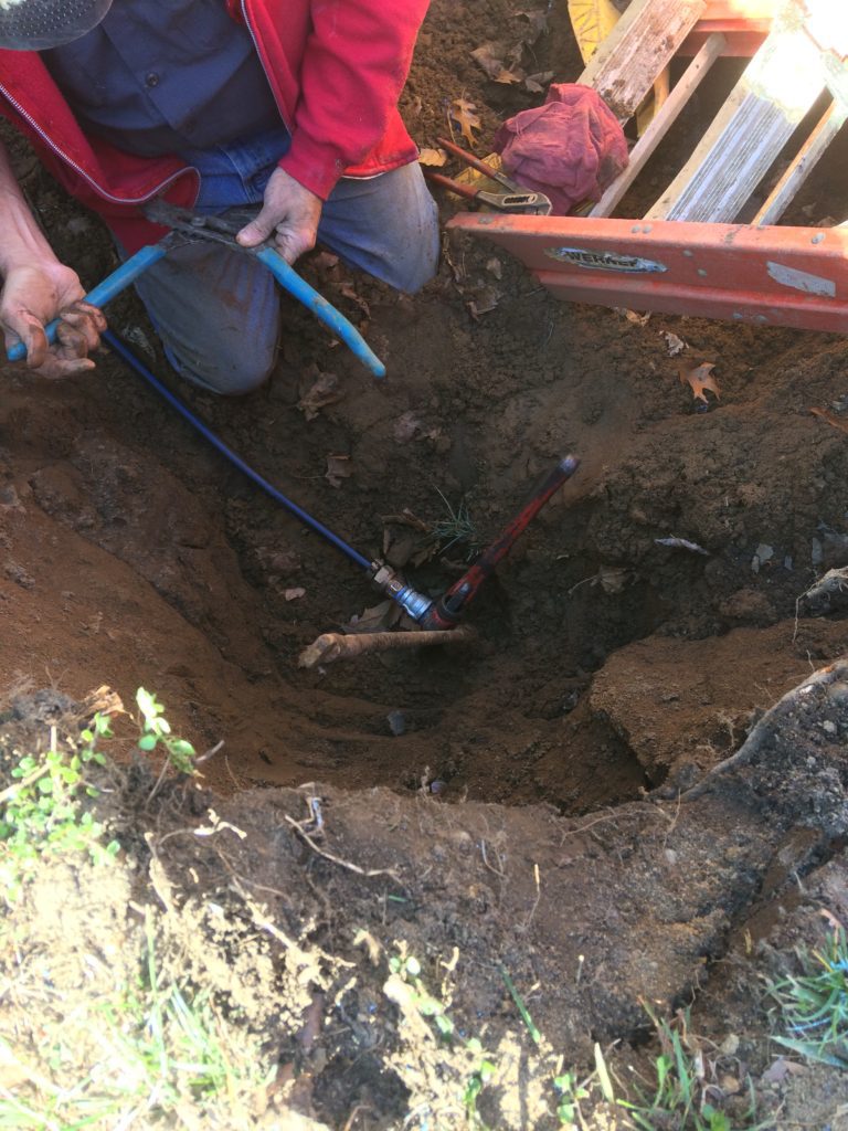 A person is digging in the ground with a blue hose.